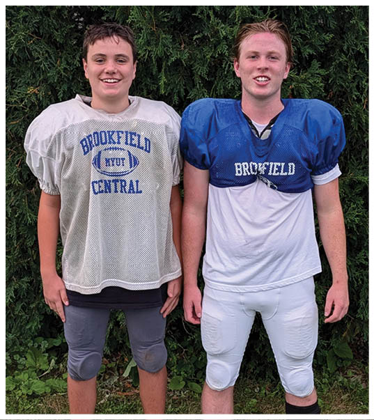 Two people wearing football jerseys with “Brookfield Central" printed on them stand side by side in front of greenery. Description generated by AI