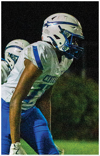 Two people in football uniforms and helmets are positioned on a grassy field at night, appearing ready to start a play. Description generated by AI