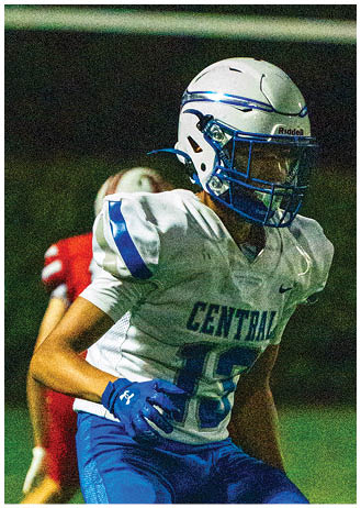A person wearing a white and blue football uniform with the word “CENTRAL" is running on a grassy field during a nighttime game. Description generated by AI