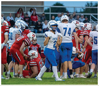 People wearing football helmets and uniforms are gathered on a field with blurred spectators in the background. Description generated by AI
