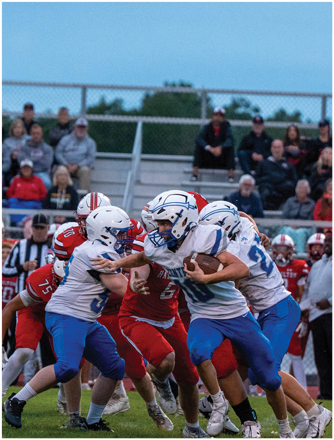 A group of people in football uniforms are actively playing on a field with some running and others attempting to block or tackle. Description generated by AI