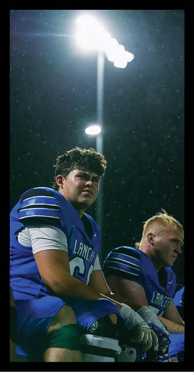 A person with curly hair is looking upward under bright stadium lights at night with small particles visible in the air. Description generated by AI