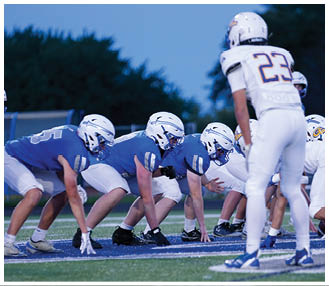 People in football uniforms are lined up on a field preparing for a play during a game. Description generated by AI