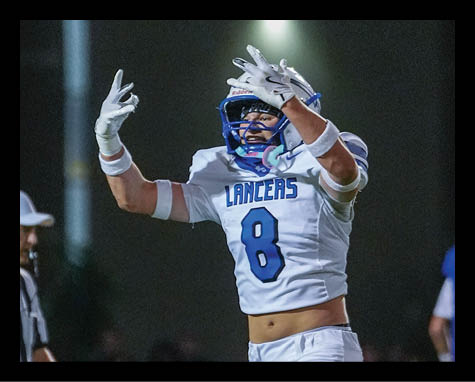 A person wearing a white football uniform with the number 8 and the word Lancers is celebrating on a field while a referee and another player in a blue and yellow uniform are in the background. Description generated by AI