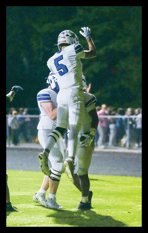 Three people in white football uniforms are celebrating on a grassy field at night with a crowd in the background. Description generated by AI