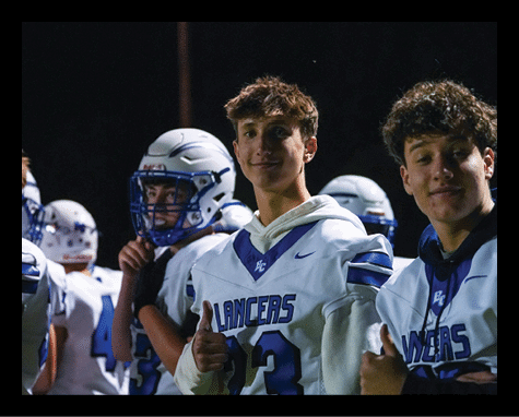 People wearing football uniforms with “Lancers" on the jerseys are standing together at night, with two of them giving thumbs up and smiling. Description generated by AI