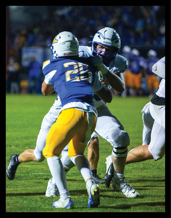 People wearing football uniforms are actively engaged in a nighttime game on a grass field with a crowd in the background. Description generated by AI