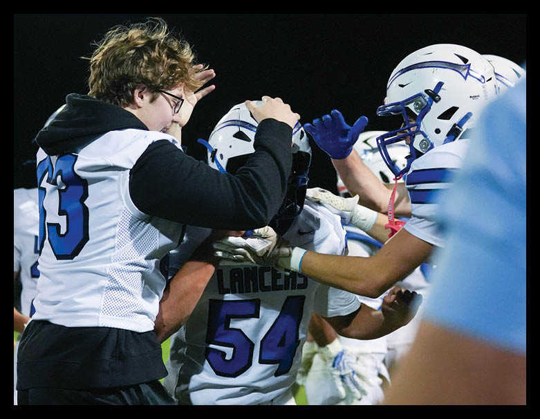 People wearing football uniforms and helmets celebrate together on a field at night. Description generated by AI