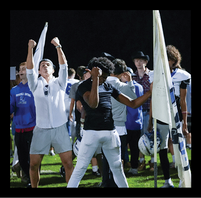 A group of people on a sports field at night are celebrating with raised fists and holding flags, with some wearing athletic gear and others in casual clothing. Description generated by AI