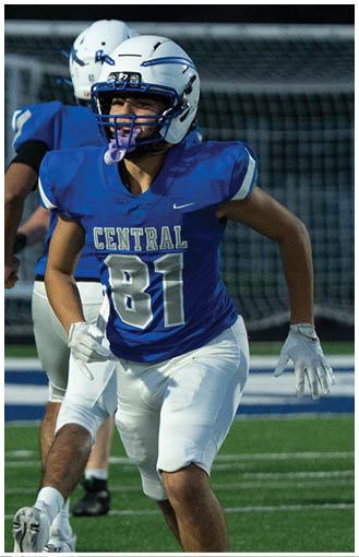 A person wearing a blue football jersey with the number 81 and the word Central is running on a football field with another player in the background. Description generated by AI