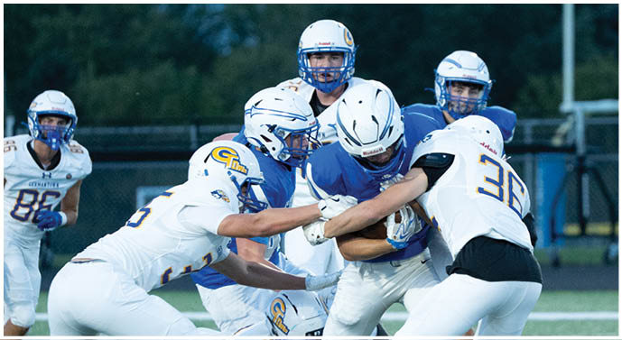 Several people in football uniforms are engaged in a tackle on a field during a game. Description generated by AI