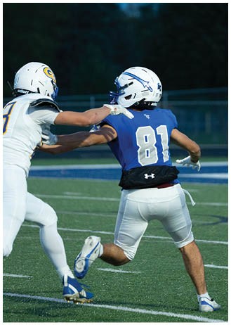 A person wearing a blue football jersey with the number 81 and a white helmet is preparing to throw a football on a field during dusk. Description generated by AI