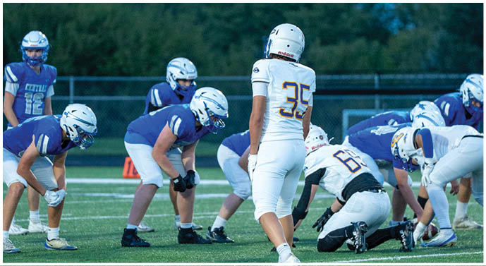 People in sports uniforms are positioned on a football field, preparing for a play. Description generated by AI
