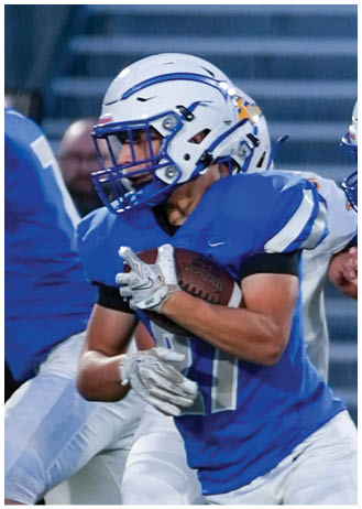 Two people in blue and white football uniforms are engaged in a play on a field with one holding a football and the other preparing to block. Description generated by AI