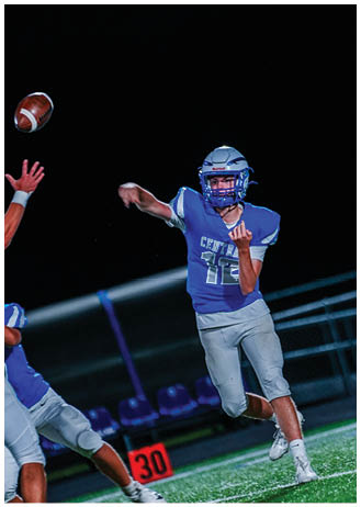 A person wearing a blue football uniform and helmet is throwing a football against a dark background. Description generated by AI
