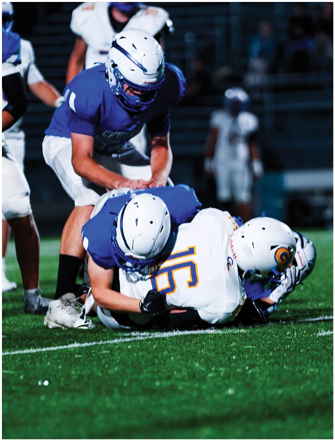 Two people in blue sports uniforms tackle a person in a white sports uniform with the number 16 on a football field during a game. Description generated by AI