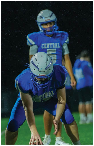 A person wearing a blue football jersey with the number 10 and a white helmet is holding a football and looking to the side during a game. Description generated by AI
