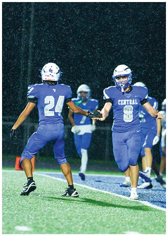 People wearing football uniforms and helmets are standing on a field, with one person in a blue jersey numbered 60 gesturing with their arm. Description generated by AI