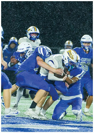 Two people in blue and white football uniforms are engaged in a play on a field with one holding a football and the other preparing to block. Description generated by AI
