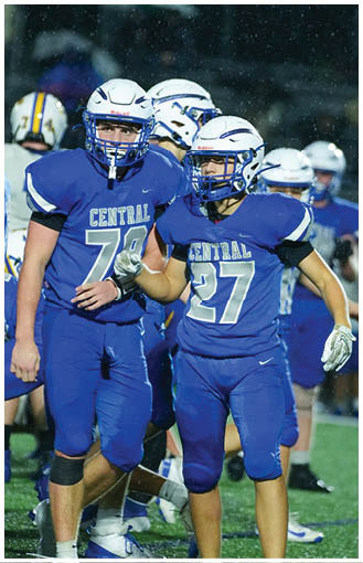A person wearing a blue football uniform and white helmet is running with a football while another person reaches out with both hands attempting to catch or tackle. Description generated by AI
