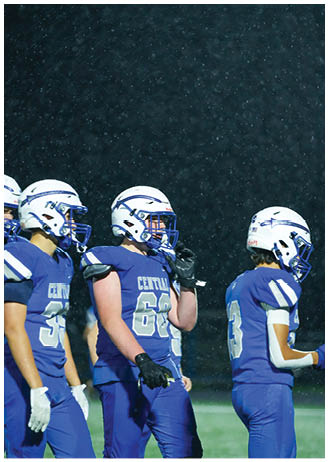 A person wearing a blue football uniform and helmet is throwing a football against a dark background. Description generated by AI