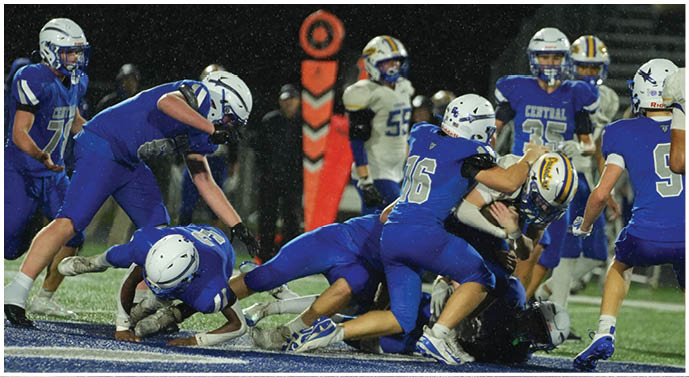 Five people wearing football helmets and uniforms are on a field at night, appearing to be in the middle of a game or practice. Description generated by AI