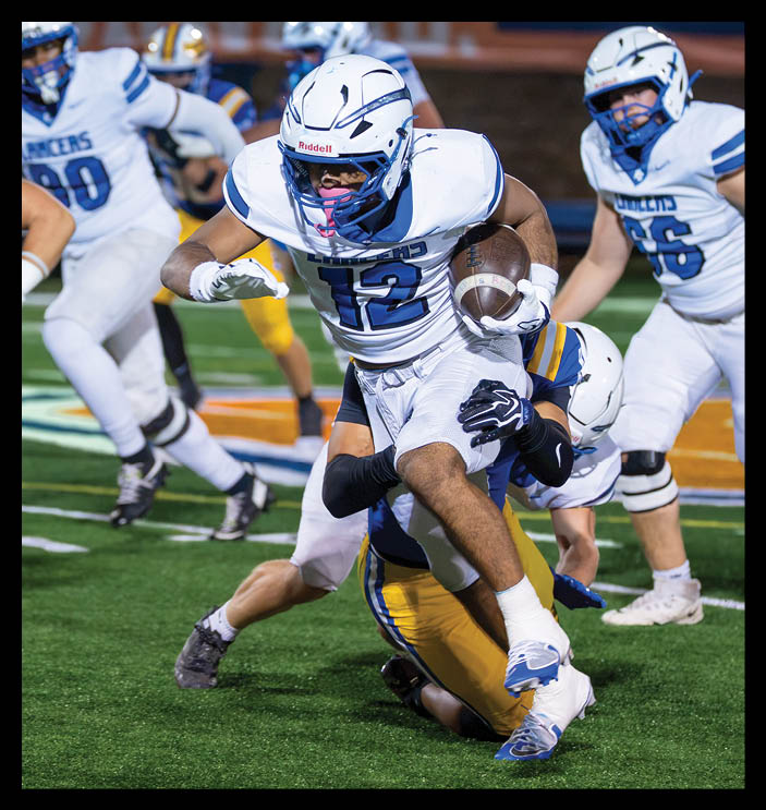 A person wearing a white football uniform with the number 12 is running with the ball while being tackled by another person in a blue and yellow uniform on a football field. Description generated by AI