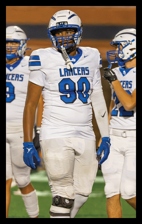 Two people wearing white football uniforms with blue accents and helmets stand on a field during a game. Description generated by AI