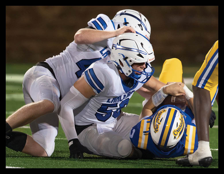 Two people wearing white and blue football uniforms are engaged in a close physical interaction during a game. Description generated by AI