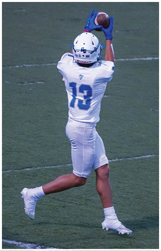 A person wearing a white football uniform with the number 13 is catching a football on a grassy field. Description generated by AI