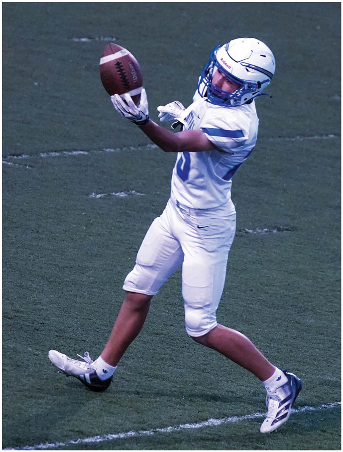 A person in white football gear and helmet is catching a football on a grassy field. Description generated by AI