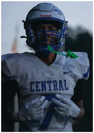A person wearing a football helmet and white jersey with “CENTRAL" and the number seven is making a hand gesture. Description generated by AI