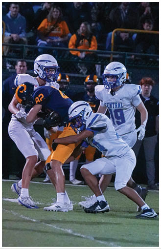 A person in a white and blue football uniform is tackling another person wearing an orange and navy uniform during a nighttime game. Description generated by AI