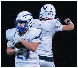 Two people wearing white sports uniforms are engaged in an athletic activity, with one person holding a ball close to their chest. Description generated by AI