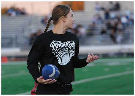 A person wearing a black shirt is holding a blue football with white laces. Description generated by AI