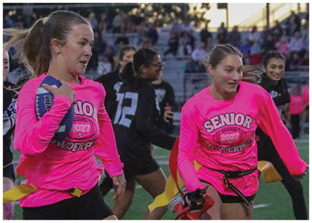 People wearing bright pink shirts are running on a sports field during an event, with some holding ribbons or batons. Description generated by AI