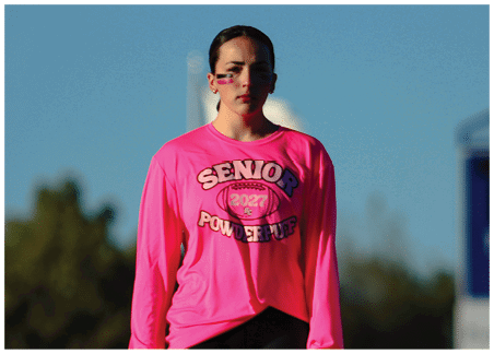 A person wearing a bright pink long-sleeve top and black leggings with a white Under Armour logo near the hip. Description generated by AI