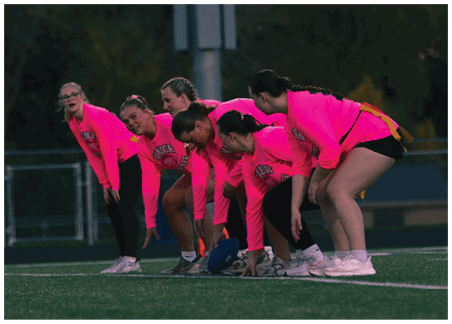 Four people wearing bright pink shirts are leaning forward closely together, appearing engaged in a shared activity or conversation. Description generated by AI