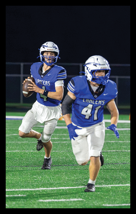 A person wearing a blue Lancers football uniform and white helmet is preparing to throw a football during a nighttime game. Description generated by AI