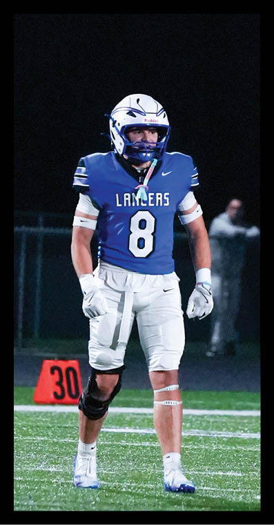 A person wearing a blue football jersey with the number 8 and white pants is standing on a football field near a yard marker at night. Description generated by AI