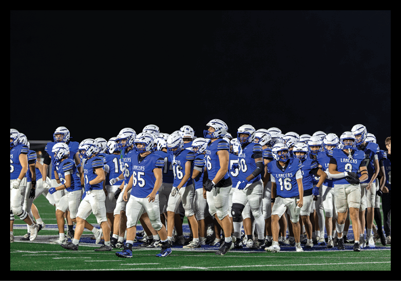 A group of people wearing blue and white football uniforms and helmets are gathered together on a field at night. Description generated by AI