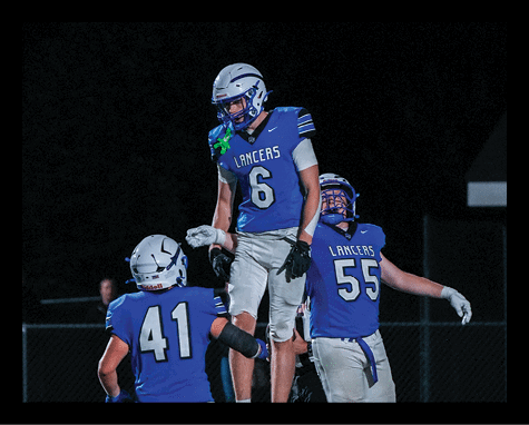Three people wearing blue football uniforms with helmets celebrate on a field at night. Description generated by AI
