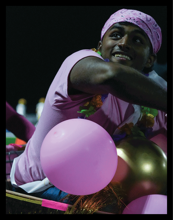 A person wearing a textured purple garment is holding a pink balloon with a small green and orange decorative item attached. Description generated by AI
