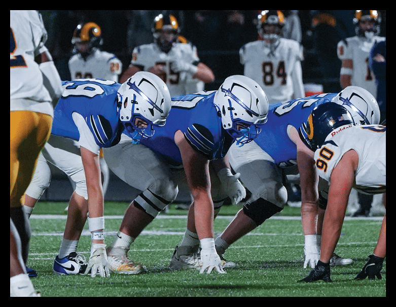 Three football players in helmets and uniforms are engaged in a close play on the field. Description generated by AI