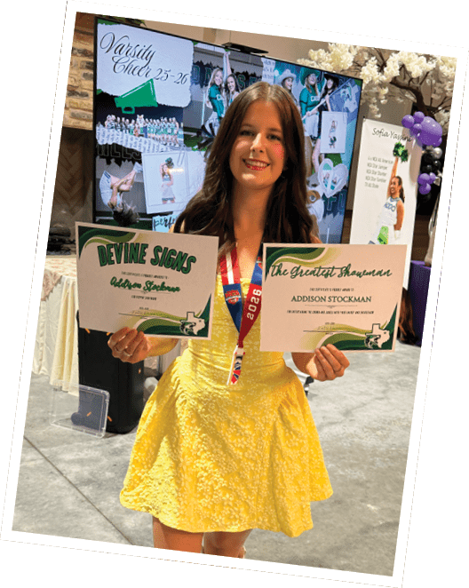 A person wearing a yellow dress and white boots is smiling and holding two award certificates in a decorated indoor space. Descripci n generada con IA