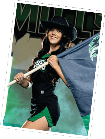 A person wearing a black outfit with green accents is holding and waving a large flag with a stylized animal logo in a smoky indoor setting. Descripci n generada con IA