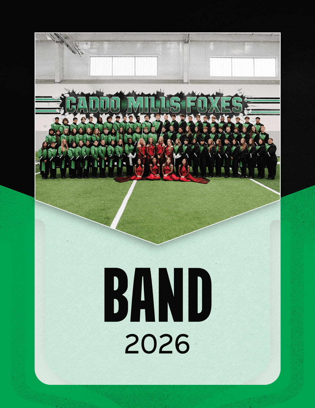 A large group of people dressed in green and black uniforms with some in red costumes pose indoors on artificial turf under a sign that reads Caddo Mills Foxes with the text Band Group Photo 2026 below. Descripci n generada con IA