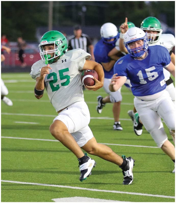 A person wearing a green helmet and white uniform with number 25 is running with a football while being chased by a person in a blue uniform with number 15 on a football field. Descripci n generada con IA
