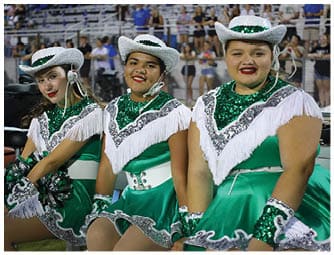 People dressed in green sequined costumes with white fringed collars and hats are standing together, likely preparing for a performance or event. Descripci n generada con IA