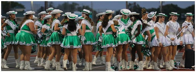 A group of people wearing green and white cheerleading uniforms with white boots are standing on a track. Descripci n generada con IA